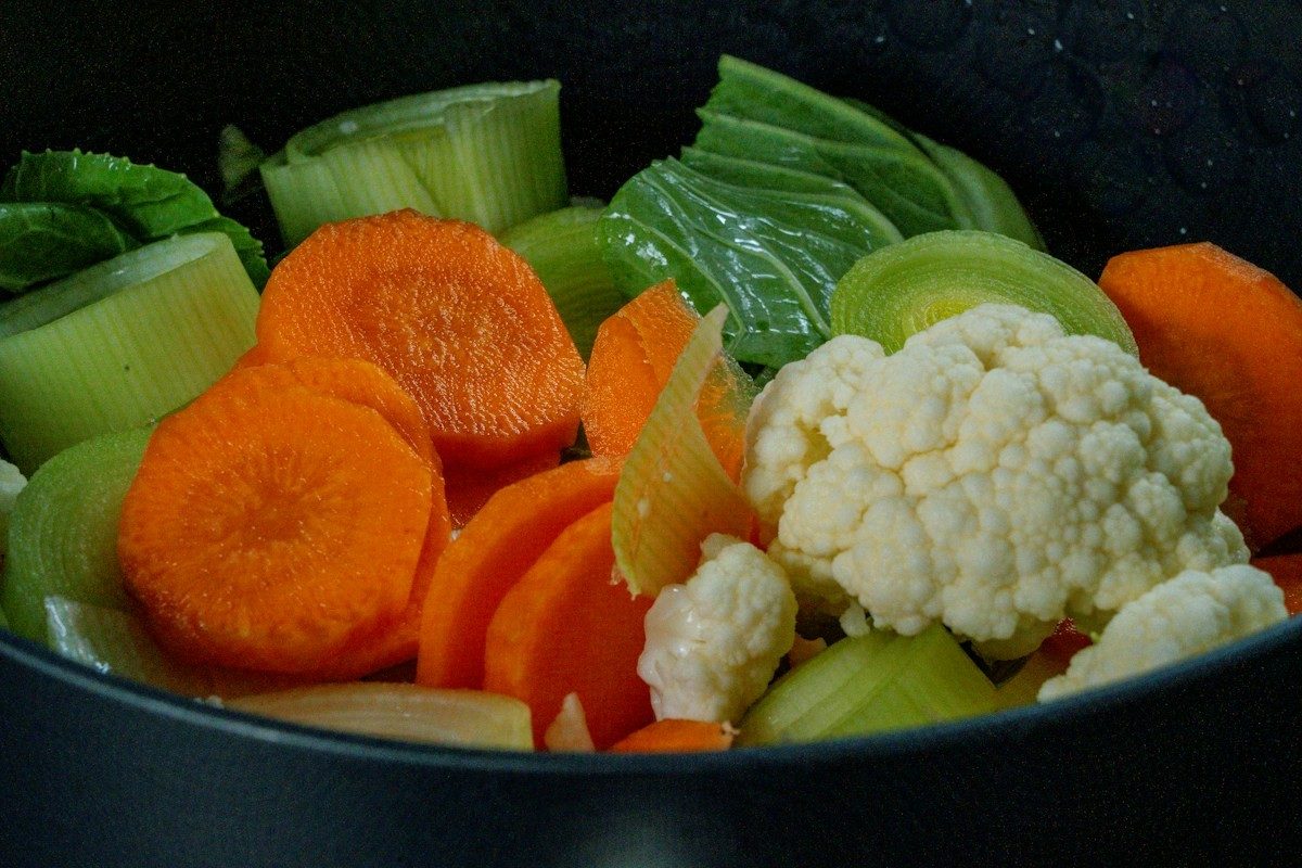 Schwarzer Topf mit Karottenscheiben, Blumenkohl und Kohl