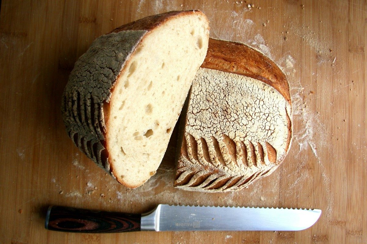 Halbierter Brotlaib mit heller Krume und einem Brotmesser auf einem Holzbrett