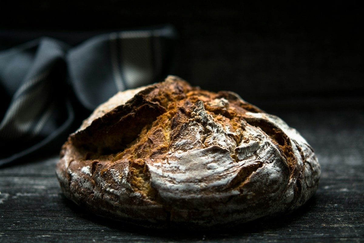 Rundes Sauerteigbrot mit dunkler, aufgerissener Kruste vor schwarzem Hintergrund