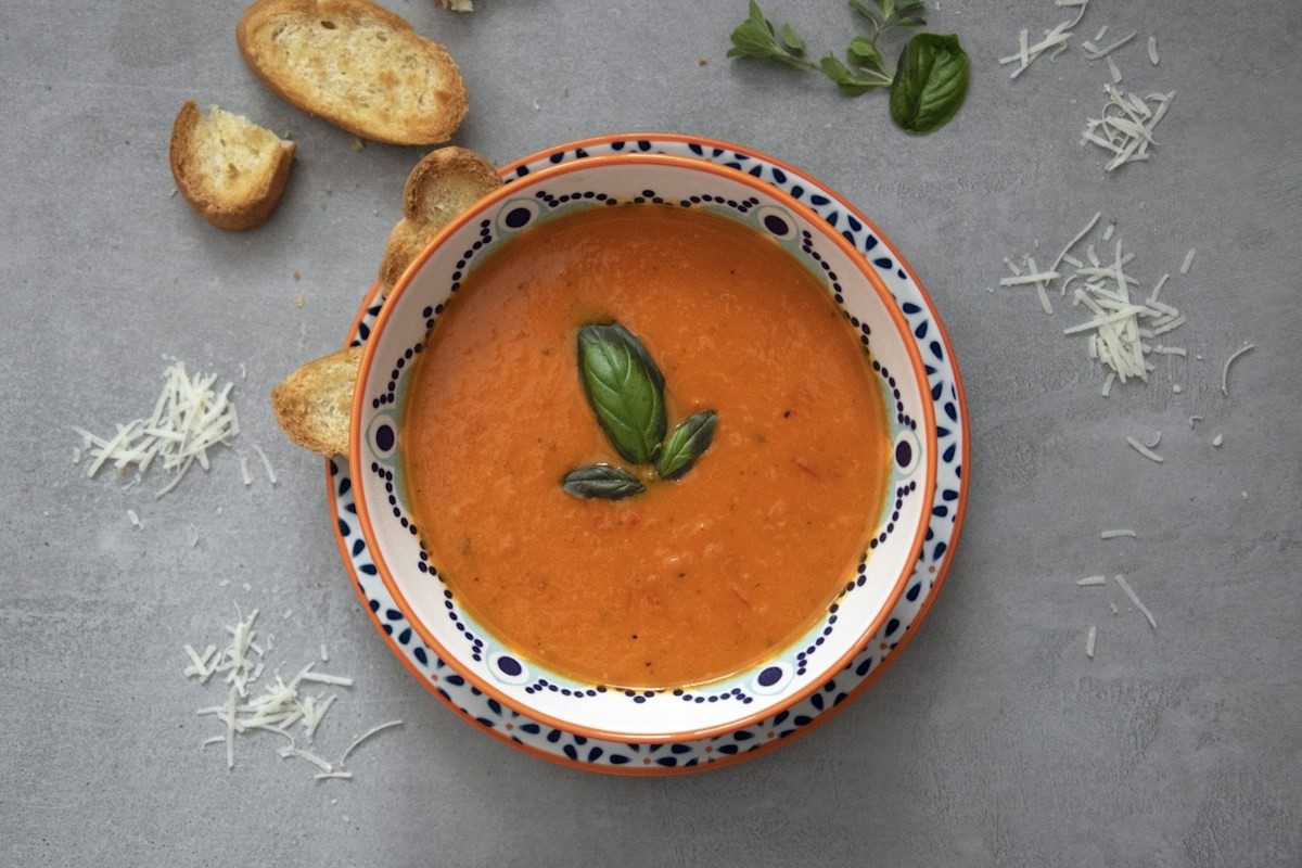 Tomatensuppe mit einem Basilikumblatt in einer gemusterten Schale, daneben Brotscheiben